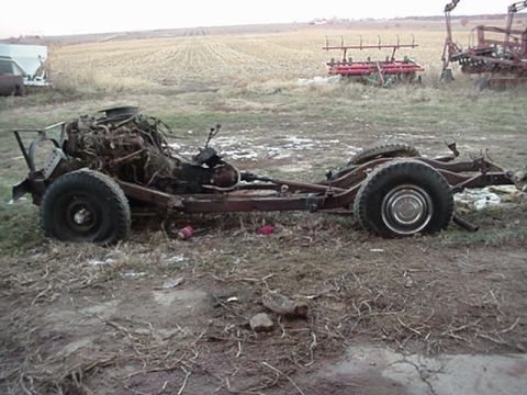 1992 Ford Bronco - The frame and engine of a vehicle are visible, resting in a grassy, open field with farm equipment in the background.