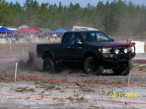 1989 Ford Bronco - A modified Toyota Tacoma navigates a dirt course, generating a cloud of dust.