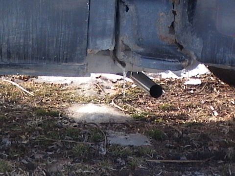 1990 Ford Bronco - The lower body panel of a vehicle shows significant rust around the exhaust pipe.