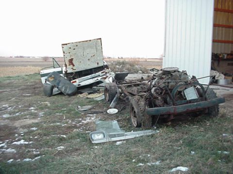 1992 Ford Bronco - Two heavily damaged vehicles, one a truck chassis with engine and the other a detached cab, lie in a field.