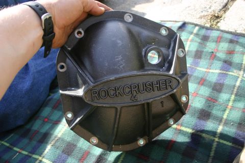 2003 Jeep TJ - A Rock Crusher differential cover is held by a person, resting on a plaid blanket outdoors.
