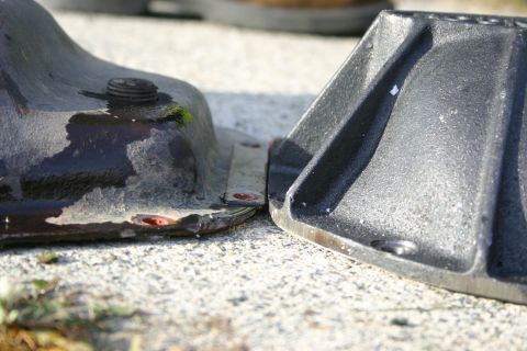 2003 Jeep TJ - Close-up of two metal wheel chocks, one dark and wet, the other gray, on a gravel surface.