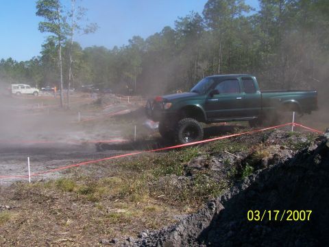 1989 Ford Bronco - A green pickup truck navigates a dusty off-road course on a sunny day.