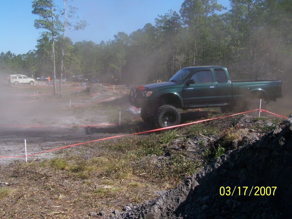 Green pickup truck with lifted suspension driving through dirt and dust
