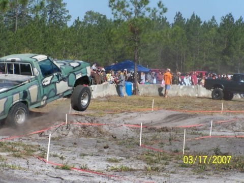 1989 Ford Bronco - A camouflaged pickup truck takes flight during an event, with a crowd watching from the sidelines.