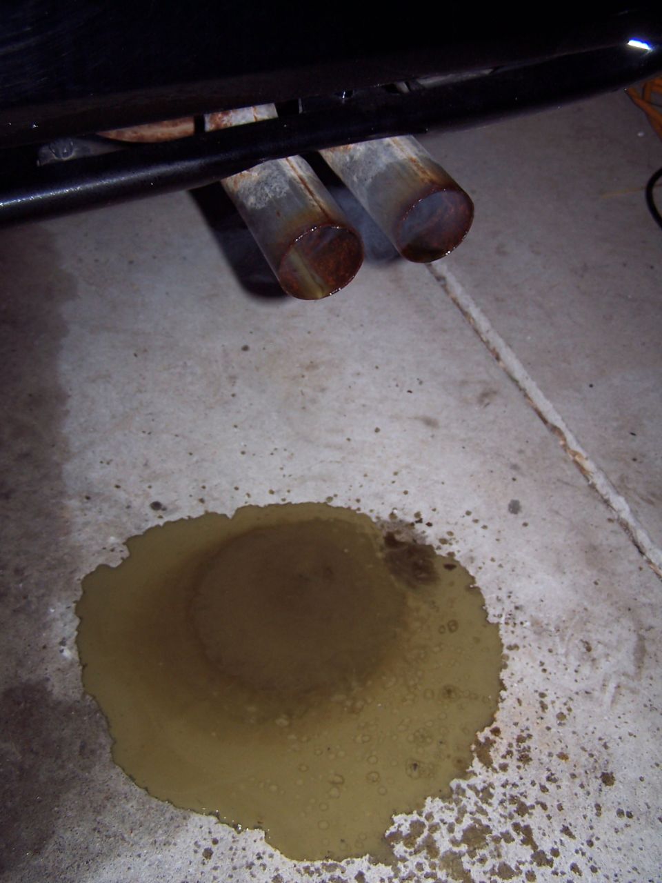Dual exhaust pipes dripping fluid onto a concrete floor