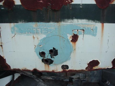 1992 Ford Bronco - A heavily rusted panel with partial text and a circular cutout is visible, showing significant wear and tear.