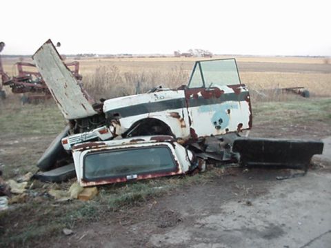 1992 Ford Bronco - This heavily damaged truck cab, possibly a Ford Bronco, sits in a field with its hood open and rear window detached.