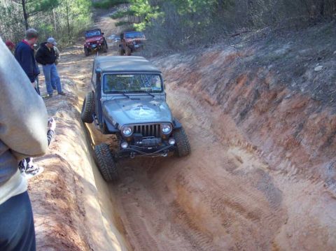 2004 Jeep Wrangler - Multiple Jeeps navigate a challenging off-road trail, with one vehicle descending into a deep rut.