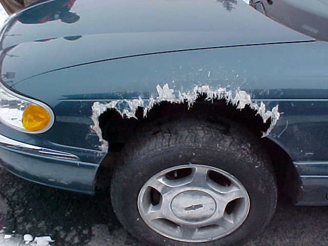 Teal car fender with large ice chunks hanging from the wheel well opening