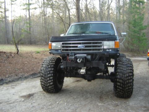 1989 Ford Bronco - This lifted black Ford truck features a prominent grille and large off-road tires, suggesting a model year around 1987.