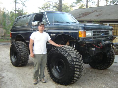 1989 Ford Bronco - A heavily modified black Ford Bronco with oversized tires is shown with a man for scale.