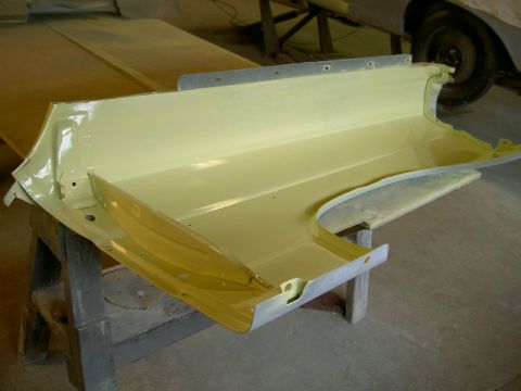 1967 Ford Ranchero - A car fender part, painted yellow, rests on sawhorses in a workshop.
