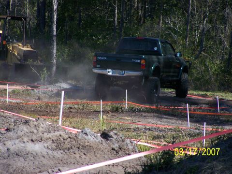 1989 Ford Bronco - A dark green Toyota Tacoma navigates an off-road course with a backhoe in the background.