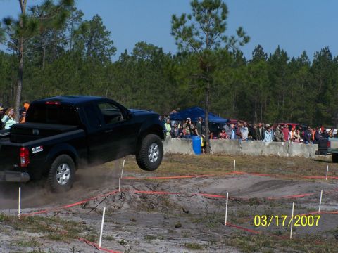 1989 Ford Bronco - Pickup truck airborne during an off-road event, with a crowd watching.