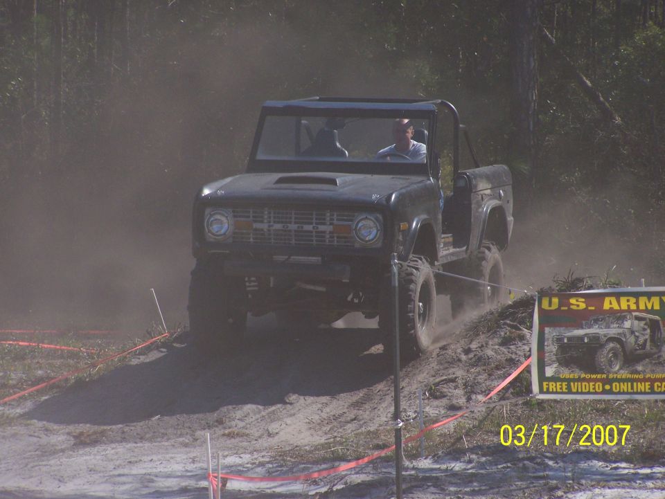 Dark Ford Bronco with top removed driving on a dirt hill, kicking up dust. U.S. Army advertisement visible