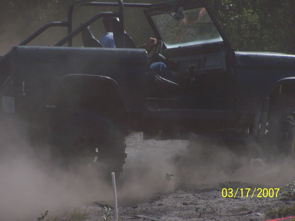 Ford Bronco kicking up dust while driving off-road. Driver visible inside