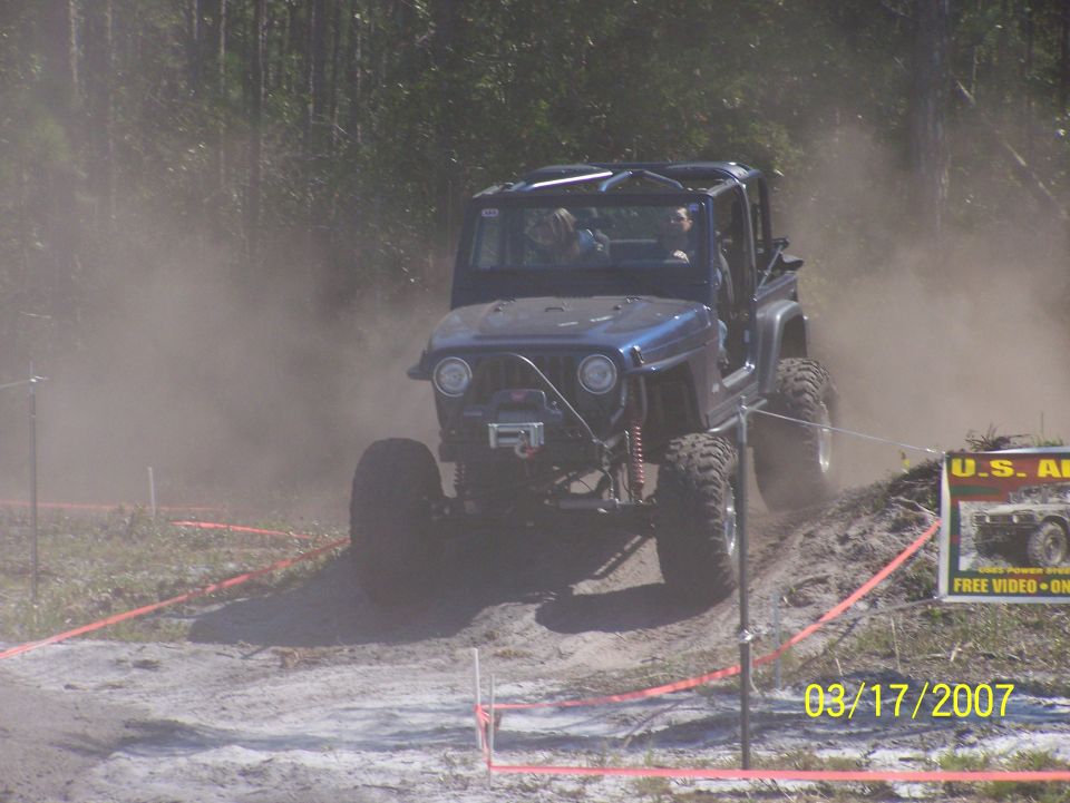 Blue off-road jeep climbing a dirt mound, dust in the air