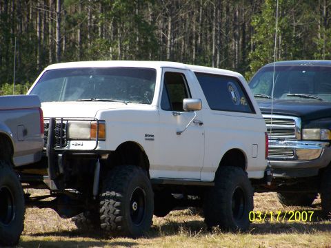 1989 Ford Bronco - A white 1989 Ford Bronco is shown with a lifted suspension and large off-road tires, parked outdoors.