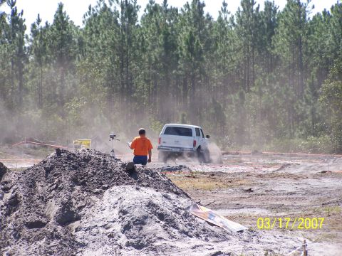 1989 Ford Bronco - A white SUV navigates a dusty off-road course, kicking up a cloud of dirt.