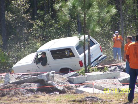 1989 Ford Bronco - A white SUV navigates a challenging off-road course, with spectators observing the action.