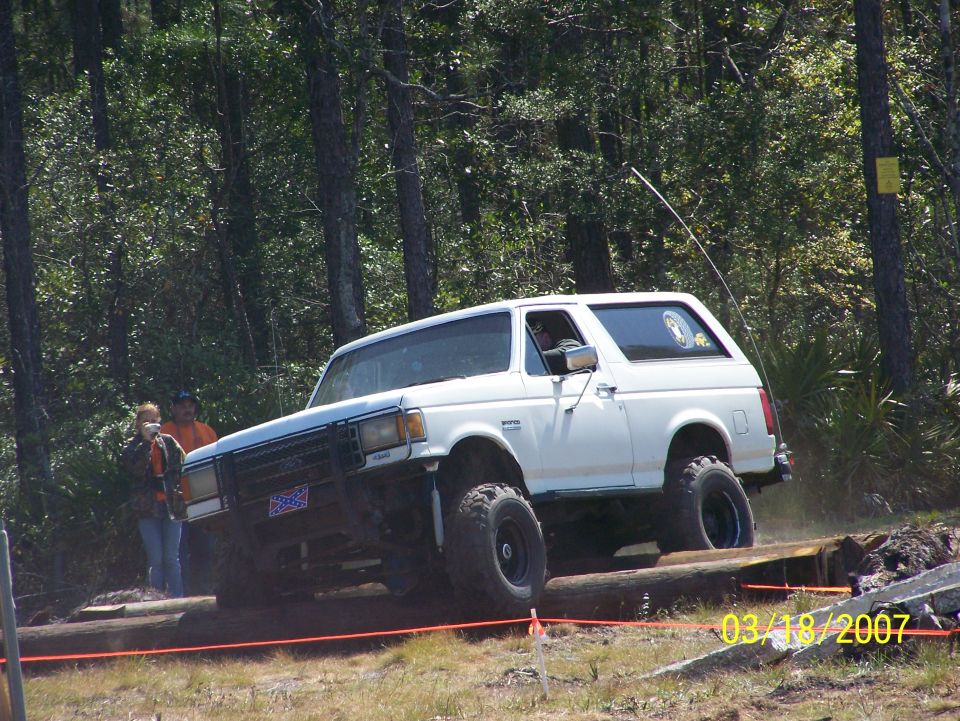 White 1989 Ford Bronco driving over logs on an off-road course