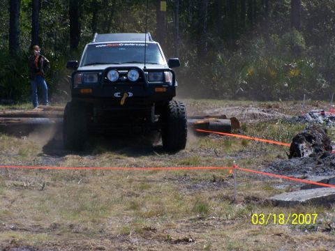 1989 Ford Bronco - A white SUV navigates an off-road course with logs and orange markers.