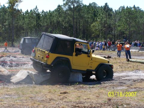 1989 Ford Bronco - A yellow Jeep navigates a challenging obstacle course with spectators observing the event.