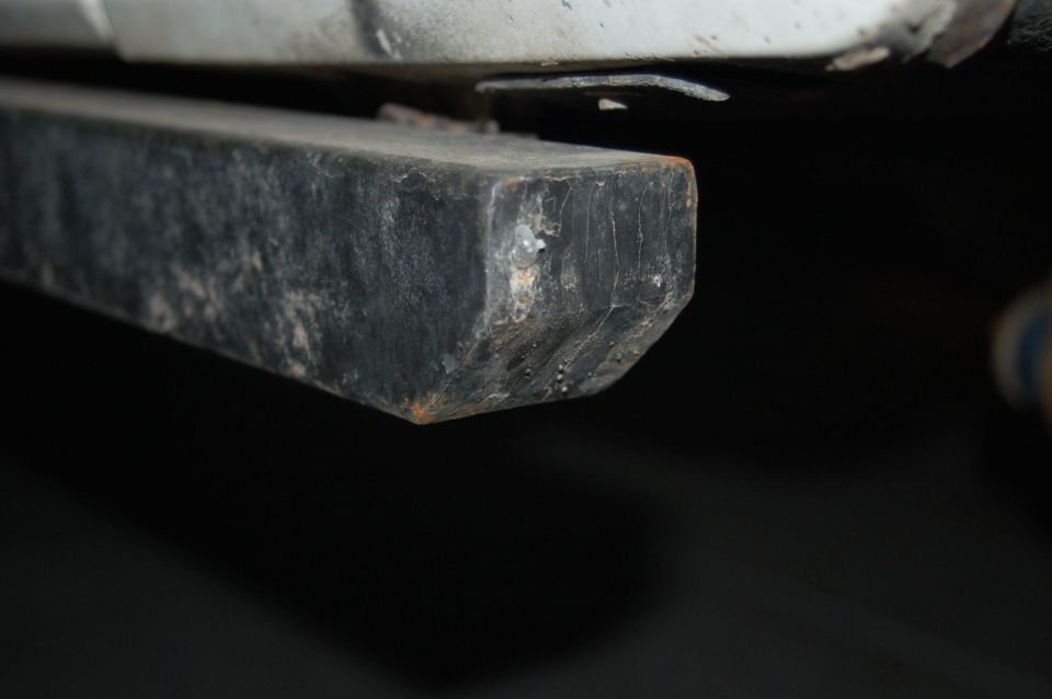 Close-up of black square steel tube slider bar end under white vehicle rocker with weld spatter