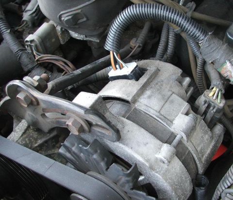 1991 Ford LTD Crown Victoria - Close-up down into an engine bay at a cast-aluminum alternator mounted on its bracket, with the serpentine belt and pulley at the bottom of…