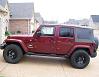 2007 Jeep Wrangler - Side view of a red 2007 Jeep Wrangler, parked on a paved driveway in front of a house.