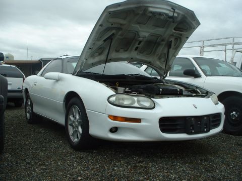 2000 Ford Crown Victoria - A white coupe, likely a 1998 Chevrolet Camaro, is parked with its hood open, revealing the engine compartment.