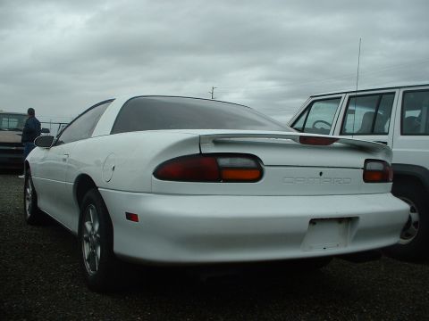 2000 Ford Crown Victoria - A white Chevrolet Camaro is parked next to a white SUV under a cloudy sky.