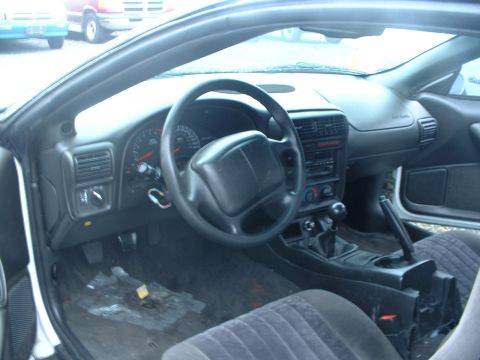 2000 Ford Crown Victoria - The interior of this vehicle shows a manual transmission shifter and worn floor mats, with other vehicles visible outside.