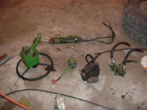 1992 Ford Bronco - Various hydraulic components and a tire are laid out on a concrete floor, suggesting a repair or parts inventory.