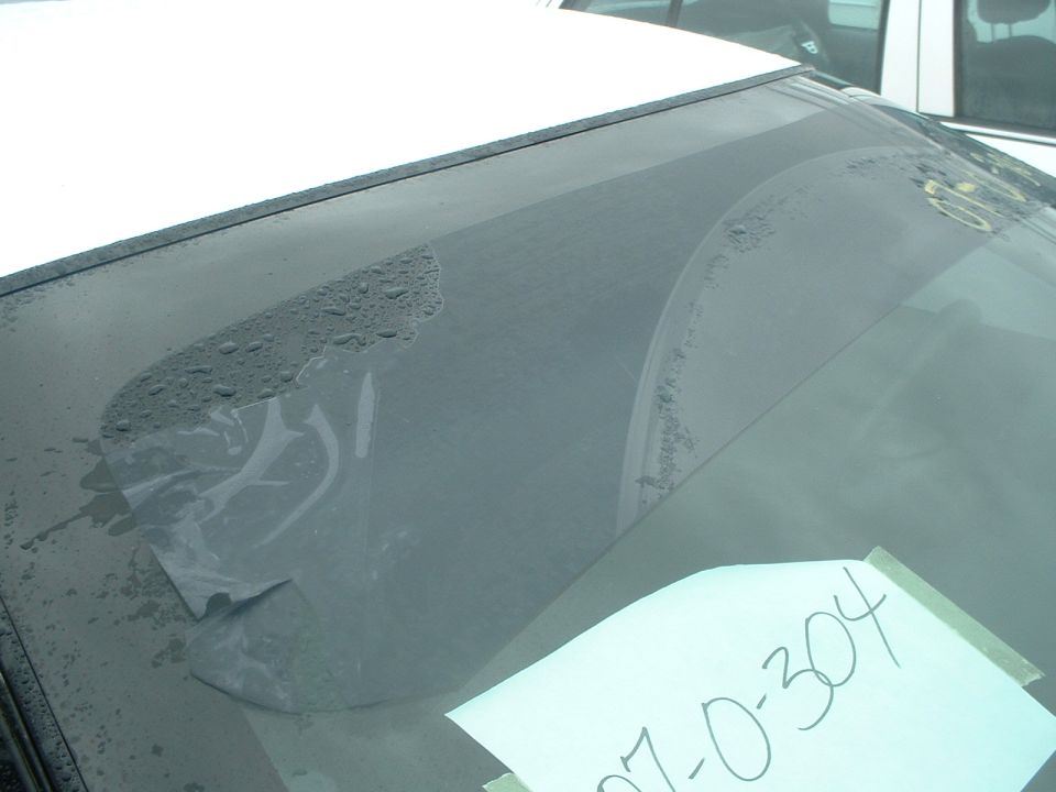 Windshield with peeling tint and water spots, paper with writing taped to it, Supermotors logo visible