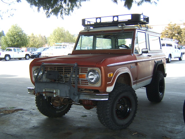 Red and white Ford Bronco with a roof rack and winch, parked outdoors