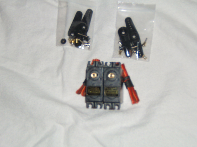 Two RC servo motors with red wires, plus two bags of black servo horns and hardware