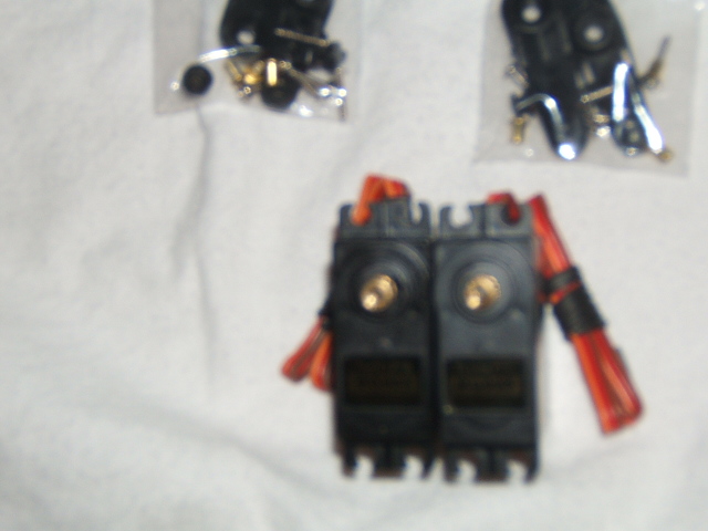 Two RC servo motors with red wires and two bags of small parts