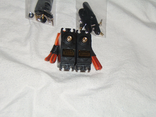 Two black servo motors labeled MG995 with orange wires and assorted hardware in plastic bags