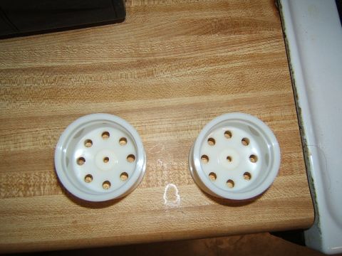 1988 Ford Bronco - Two white plastic wheels, likely for an RC crawler, sit on a wooden surface.