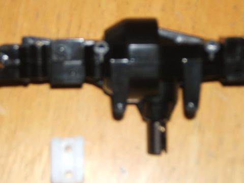 1988 Ford Bronco - Close-up of a black plastic axle assembly, likely for an RC vehicle, with a small white bracket on a wooden surface.