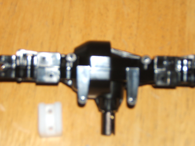 Black RC crawler axle assembly with silver suspension mounts and a white plastic bracket
