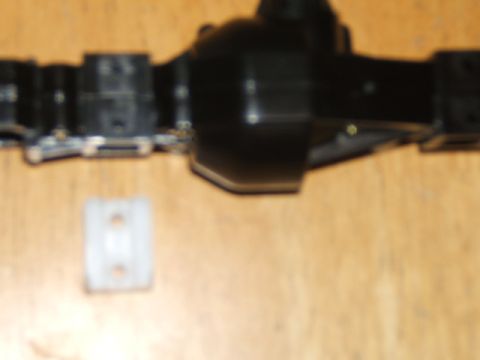 1988 Ford Bronco - Close-up of a black RC crawler axle assembly and a separate white plastic component.
