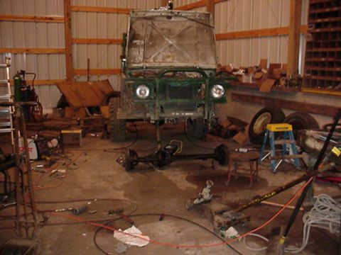 1992 Ford Bronco - A green off-road vehicle is undergoing repairs in a garage, with its front axle detached and lying on the floor.