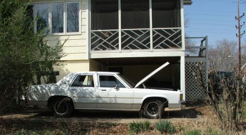 1991 Ford LTD Crown Victoria - A white sedan, likely a Ford Crown Victoria, sits parked in front of a house with its hood ajar.