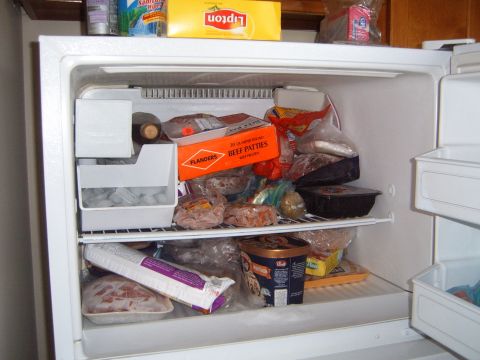 1988 Ford Bronco - The inside of a refrigerator is packed with various frozen food items and ice cubes.