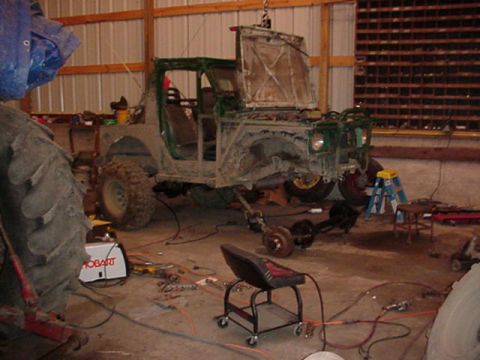 1992 Ford Bronco - A Jeep CJ-7 body is suspended in a workshop, surrounded by tools and parts for repair.