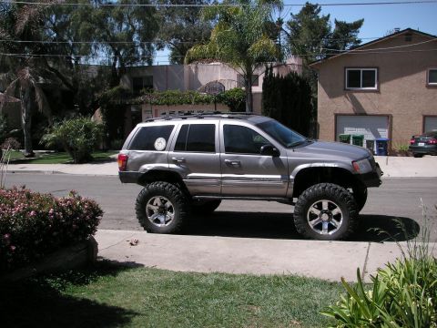 1999 Jeep Grand Cherokee - This lifted Jeep Grand Cherokee, likely from the early 2000s, sits on a residential street with modified suspension.