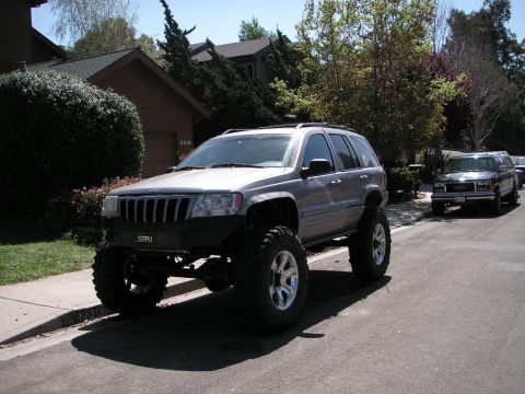 1999 Jeep Grand Cherokee - Modified 1999 Jeep Grand Cherokee with significant lift and oversized tires sits on a residential street.